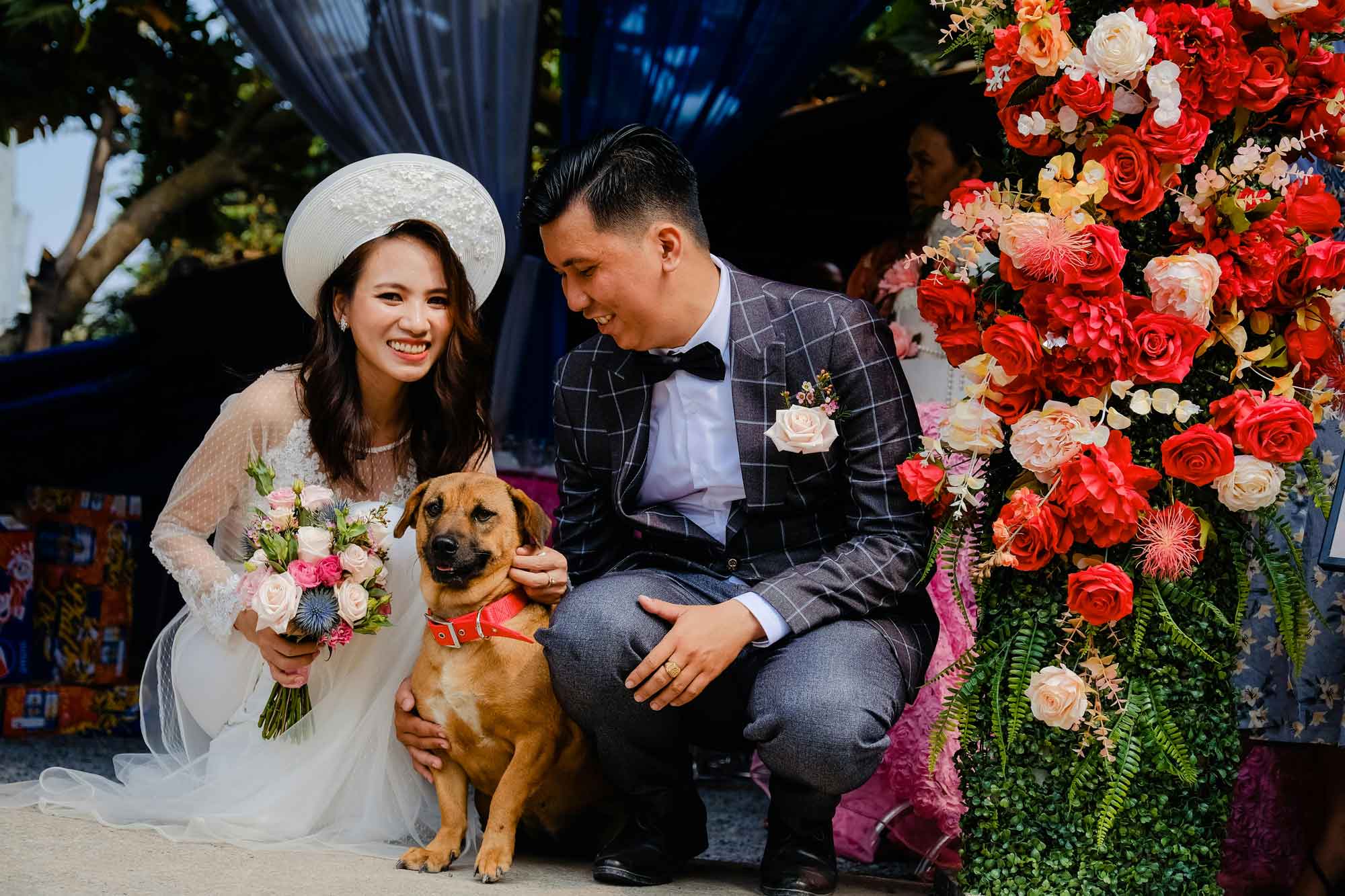 bride and groom with dog on wedding day in front of floral arch
